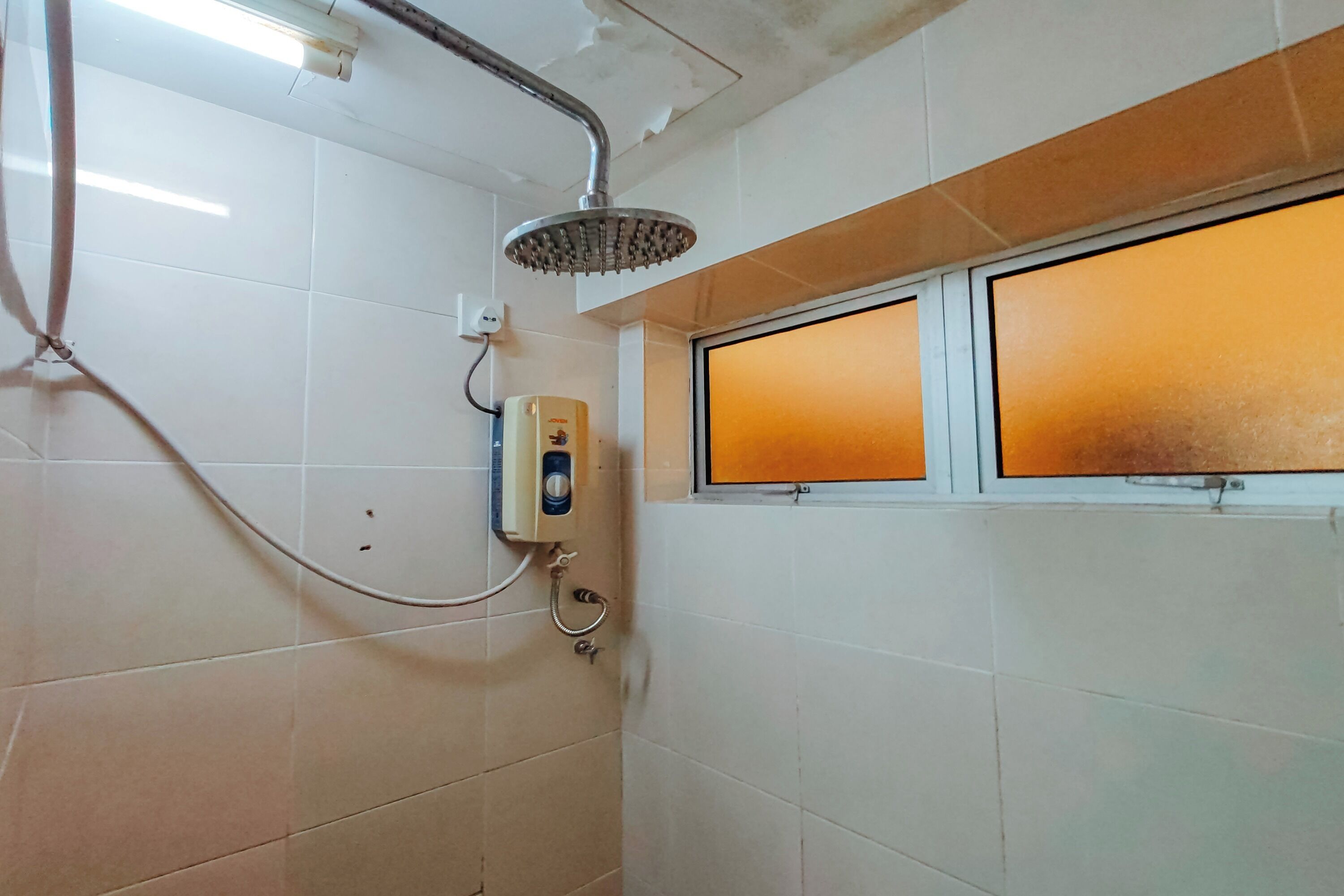 A bathroom with white tiles, a shower with a handheld showerhead, and a window with a frosted glass panel.