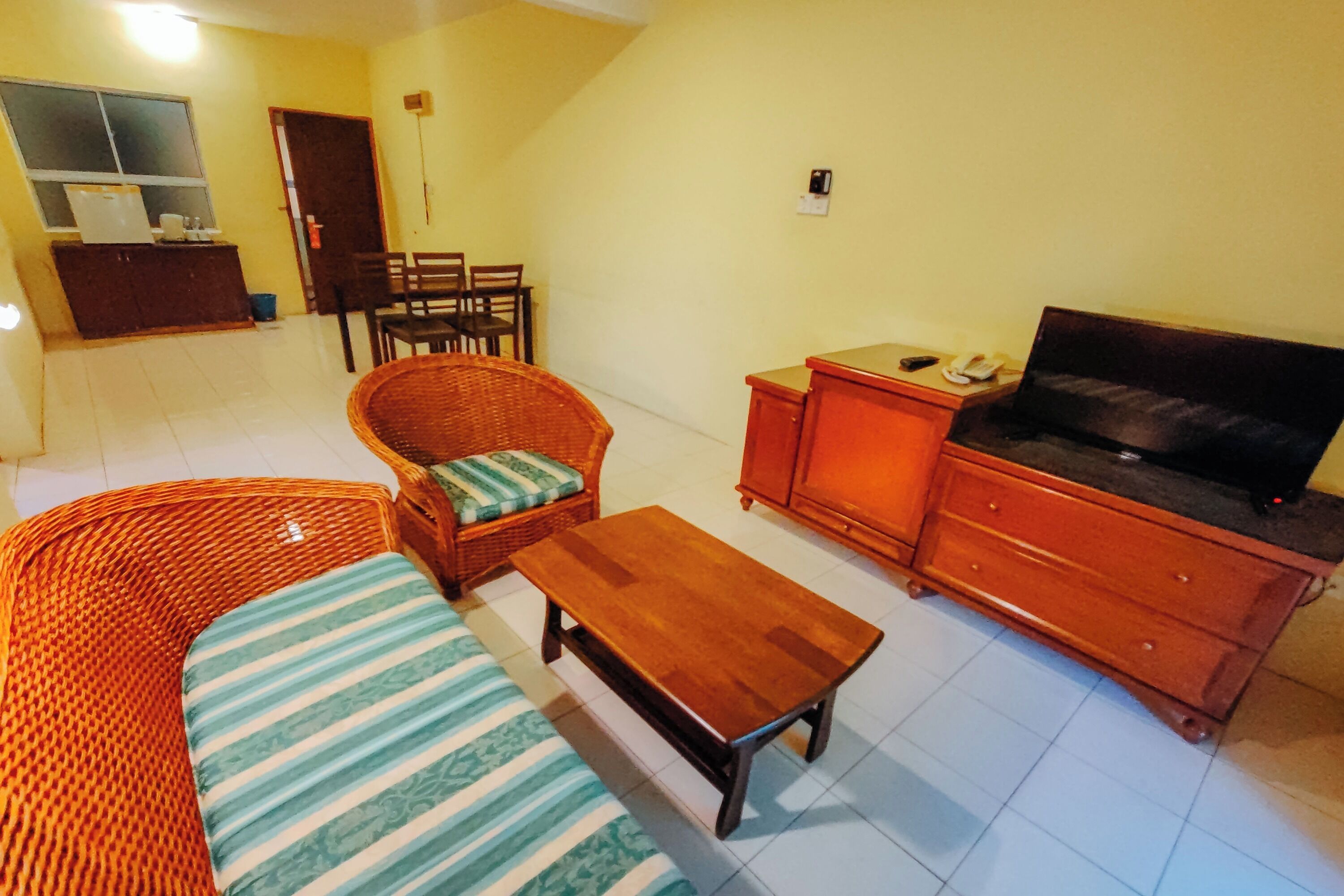 A living room with a sofa, a wooden coffee table, a television on a cabinet, and a dining area with chairs and a table.