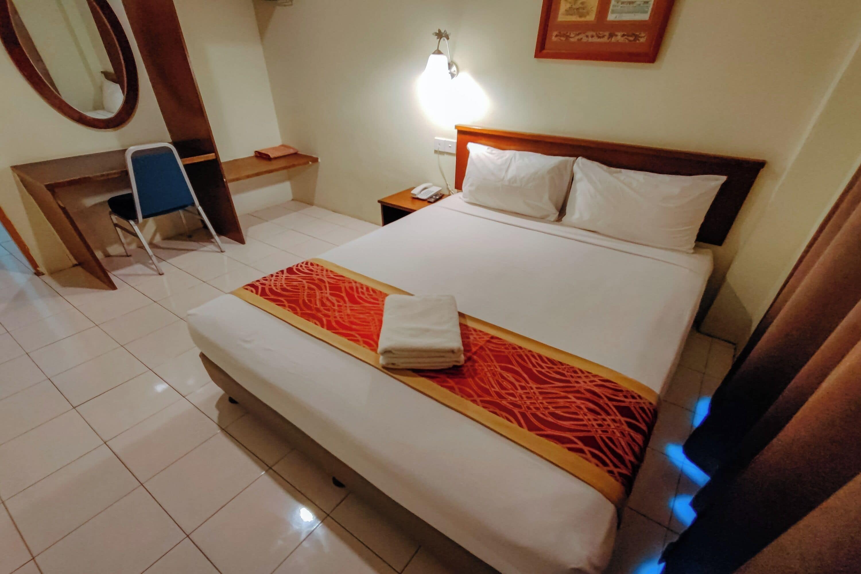 Ein Hotelzimmer mit Bett, Schreibtisch, Stuhl, Nachttisch, Lampe und Spiegel.