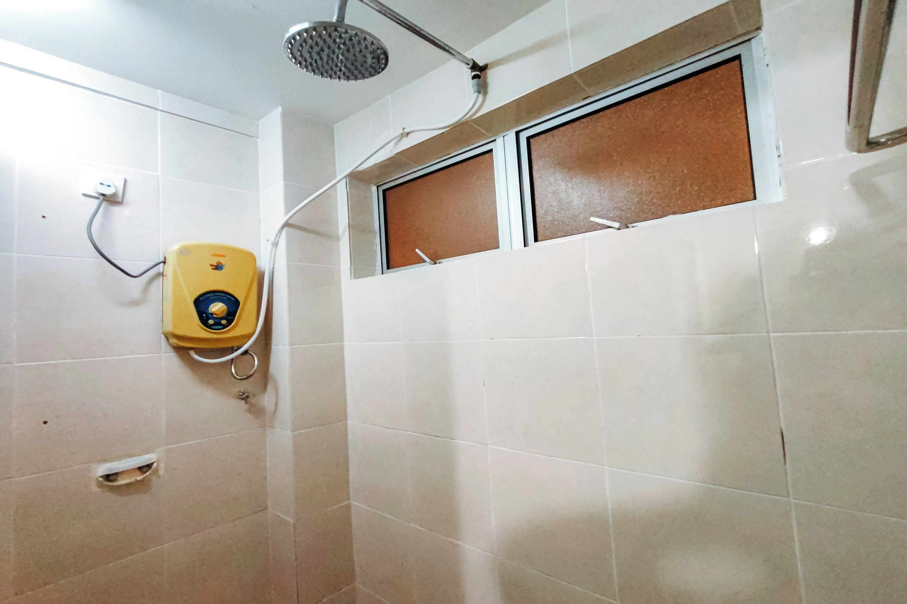 Un baño con inodoro amarillo, cabezal de ducha y ventana con persiana marrón.