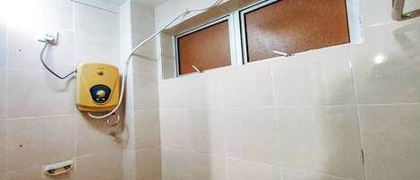 A bathroom with a yellow toilet, a showerhead, and a window with a brown blind.