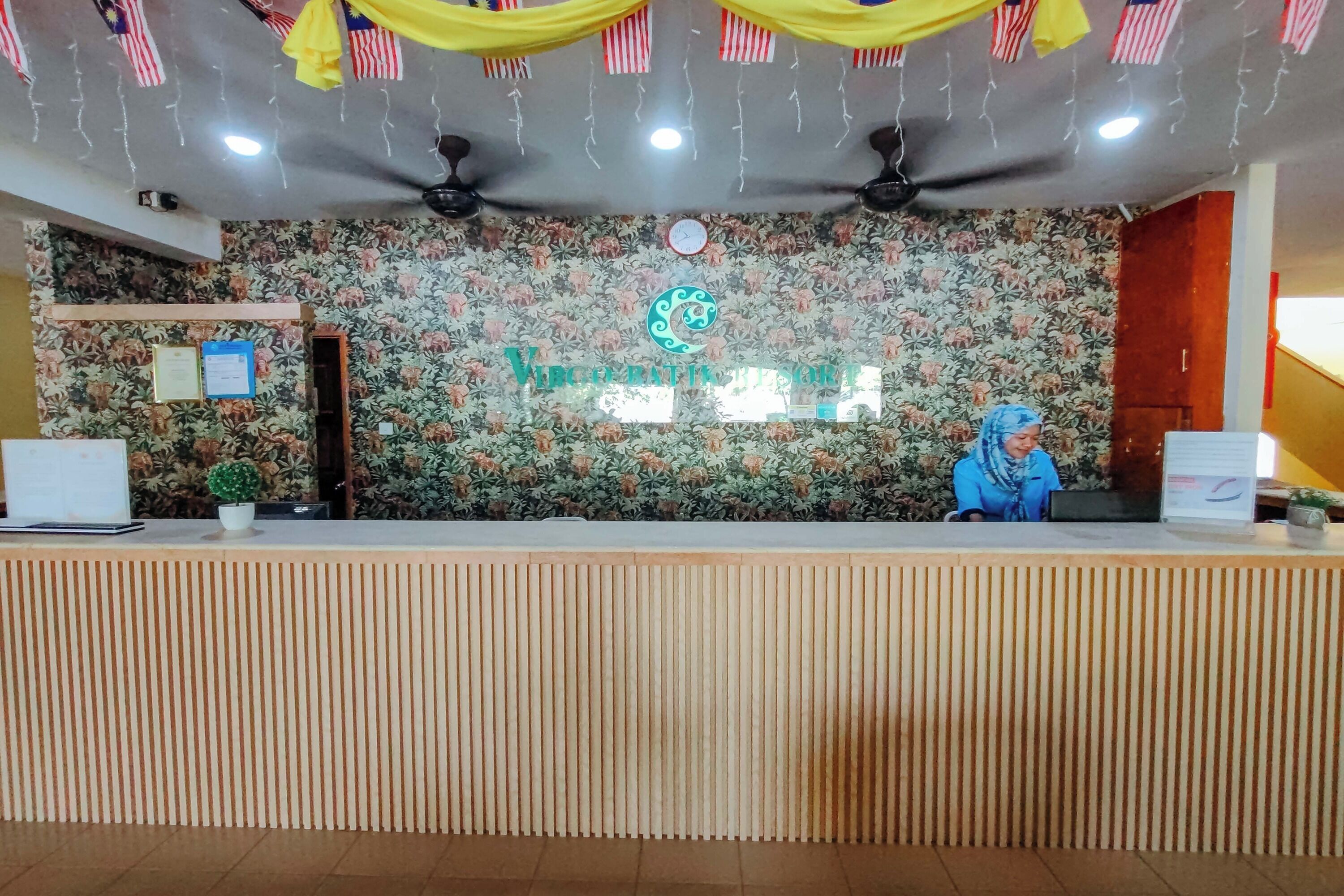 A reception desk with a floral wallpaper background, a clock, and a logo.