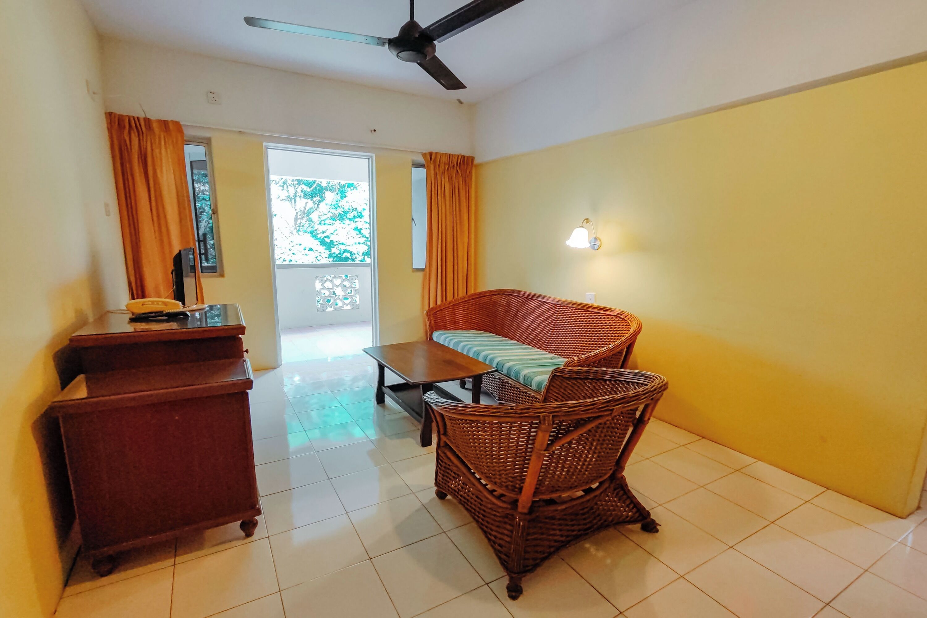 A room with a wicker sofa, a wooden cabinet, and a ceiling fan.