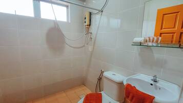 A bathroom with a toilet, sink, and shower. There is a window above the toilet, a towel hanging on the sink, and a shelf with toiletries.