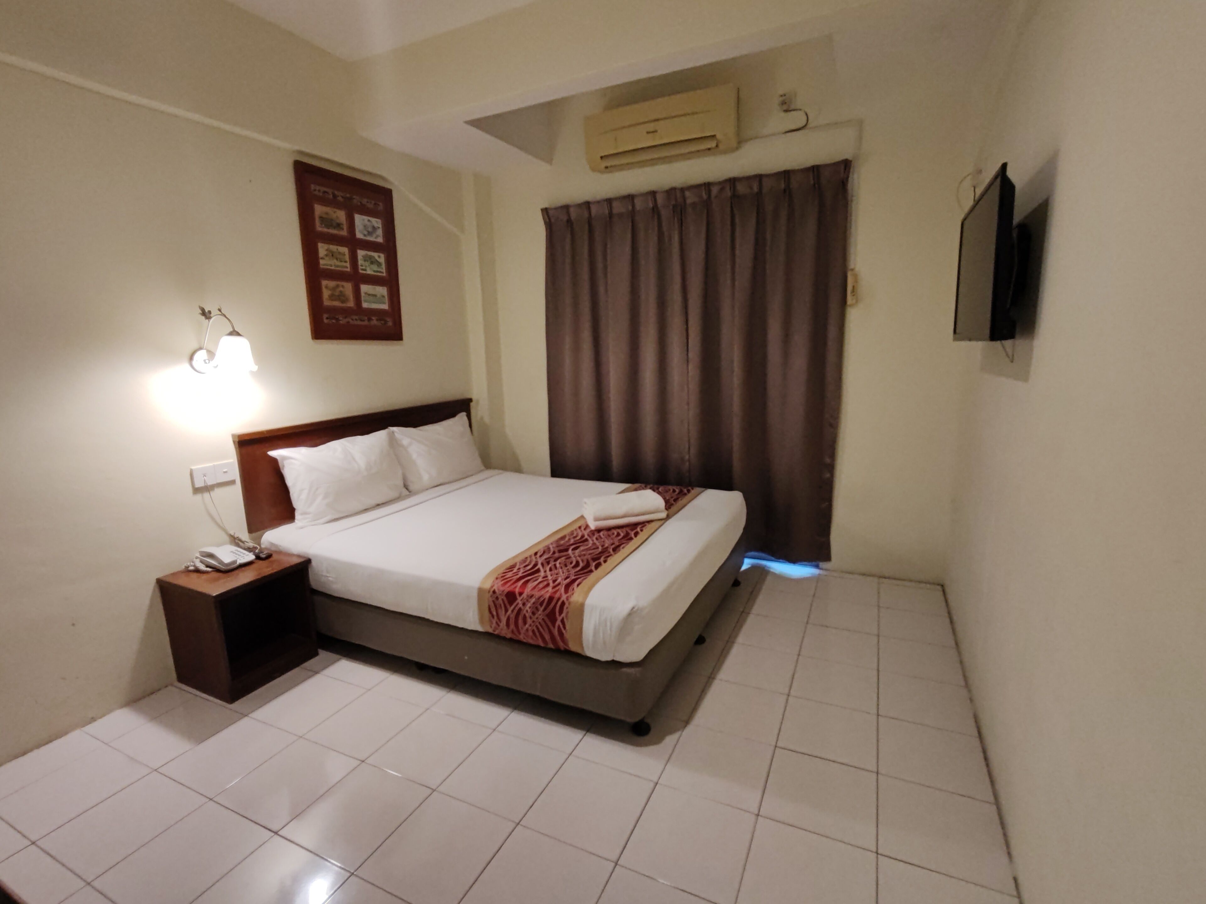 Une chambre d’hôtel équipée d’un lit, d’une table de chevet avec un téléphone, d’un climatiseur mural et d’un téléviseur à écran plat.