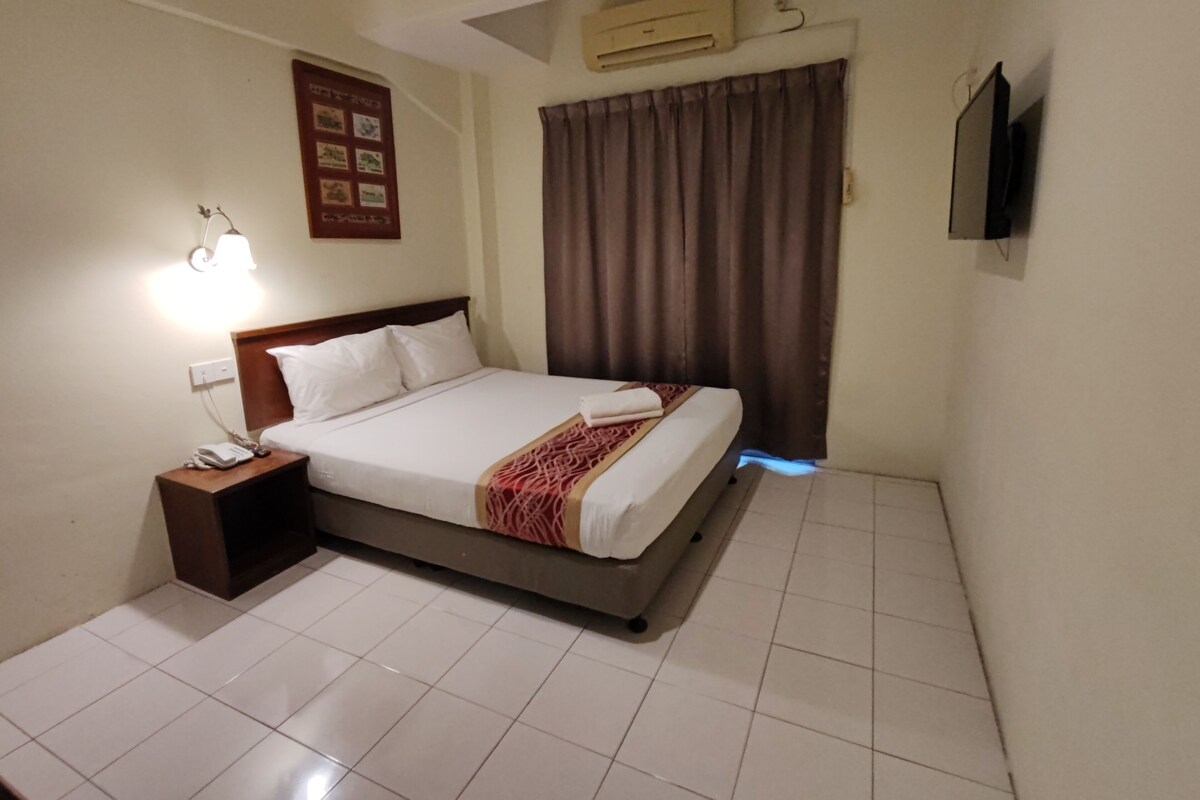 Habitación de hotel con una cama, una mesita de noche con teléfono, aire acondicionado en la pared y una televisión de pantalla plana.