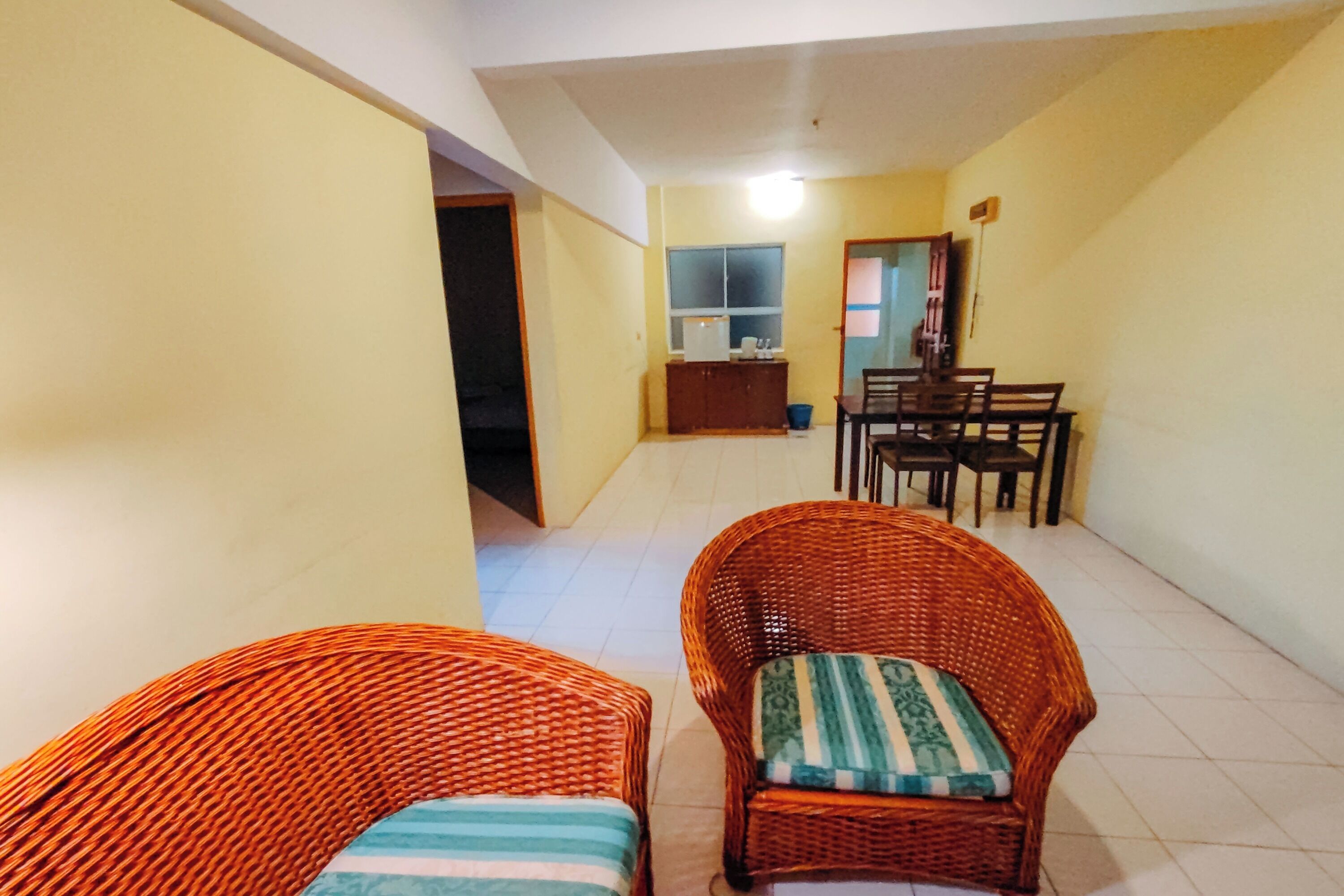 A room with two wicker chairs, a dining table, and a kitchen area in the background.