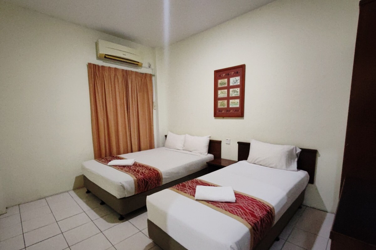 Habitación de hotel con dos camas, aire acondicionado instalado en la pared, un cuadro enmarcado y piso de baldosas.
