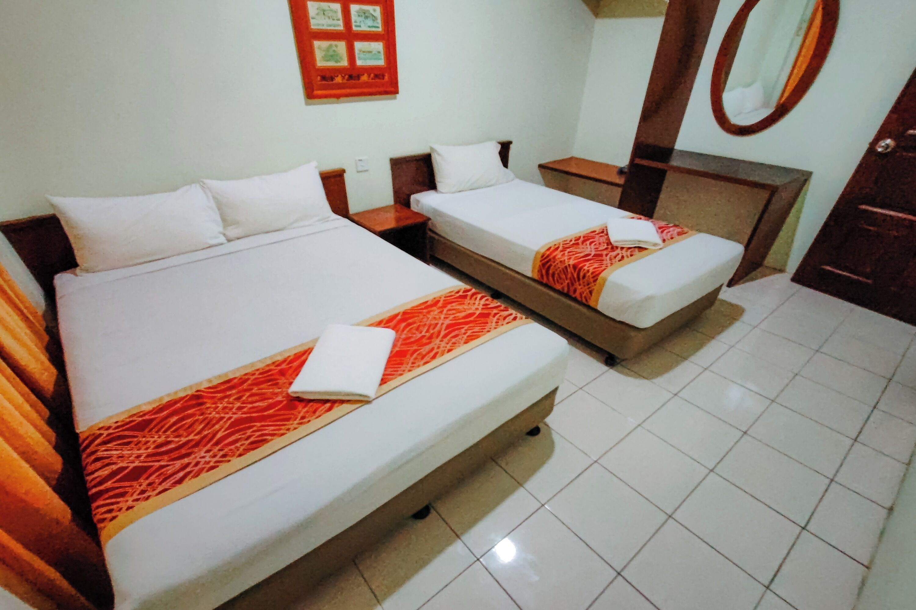 Habitación de hotel con dos camas individuales, cabecera de madera, espejo y suelo de baldosas.