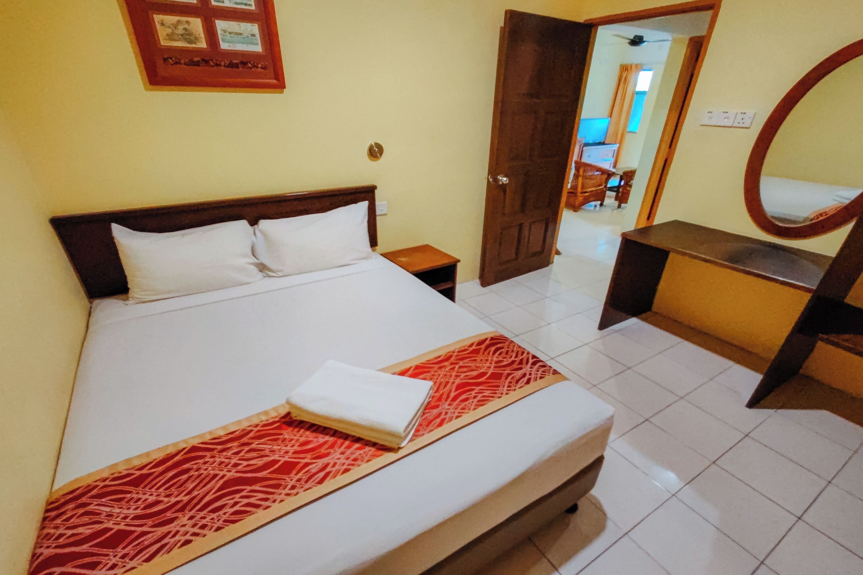 A hotel room with a bed, a bedside table, a mirror, and a door leading to another room.