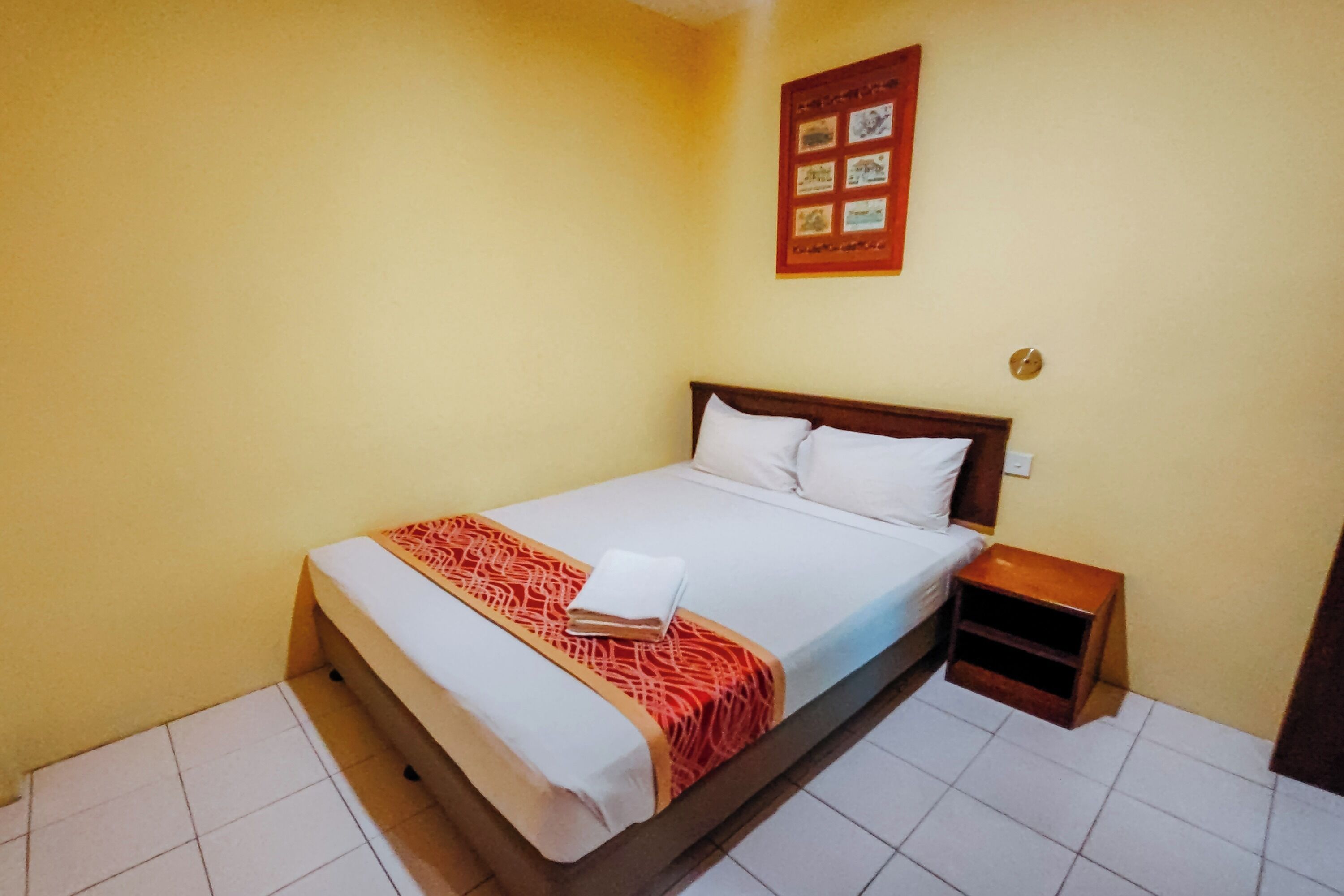 A single-bed room with a wooden headboard, a bedside table, and a wall-mounted picture frame.