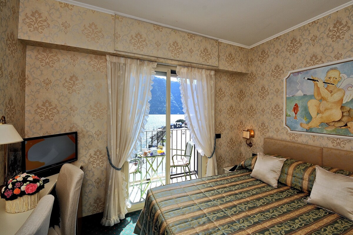 A hotel room with a bed, a TV, a chair, a table with a bouquet of flowers, and a painting on the wall.
