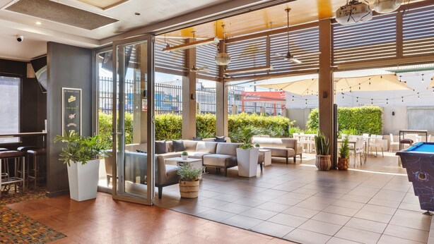 A spacious indoor/outdoor lounge area with seating, potted plants, and a pool table.
