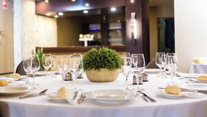 A round dining table set with white tablecloth, plates, cutlery, and wine glasses, centered with a potted plant.