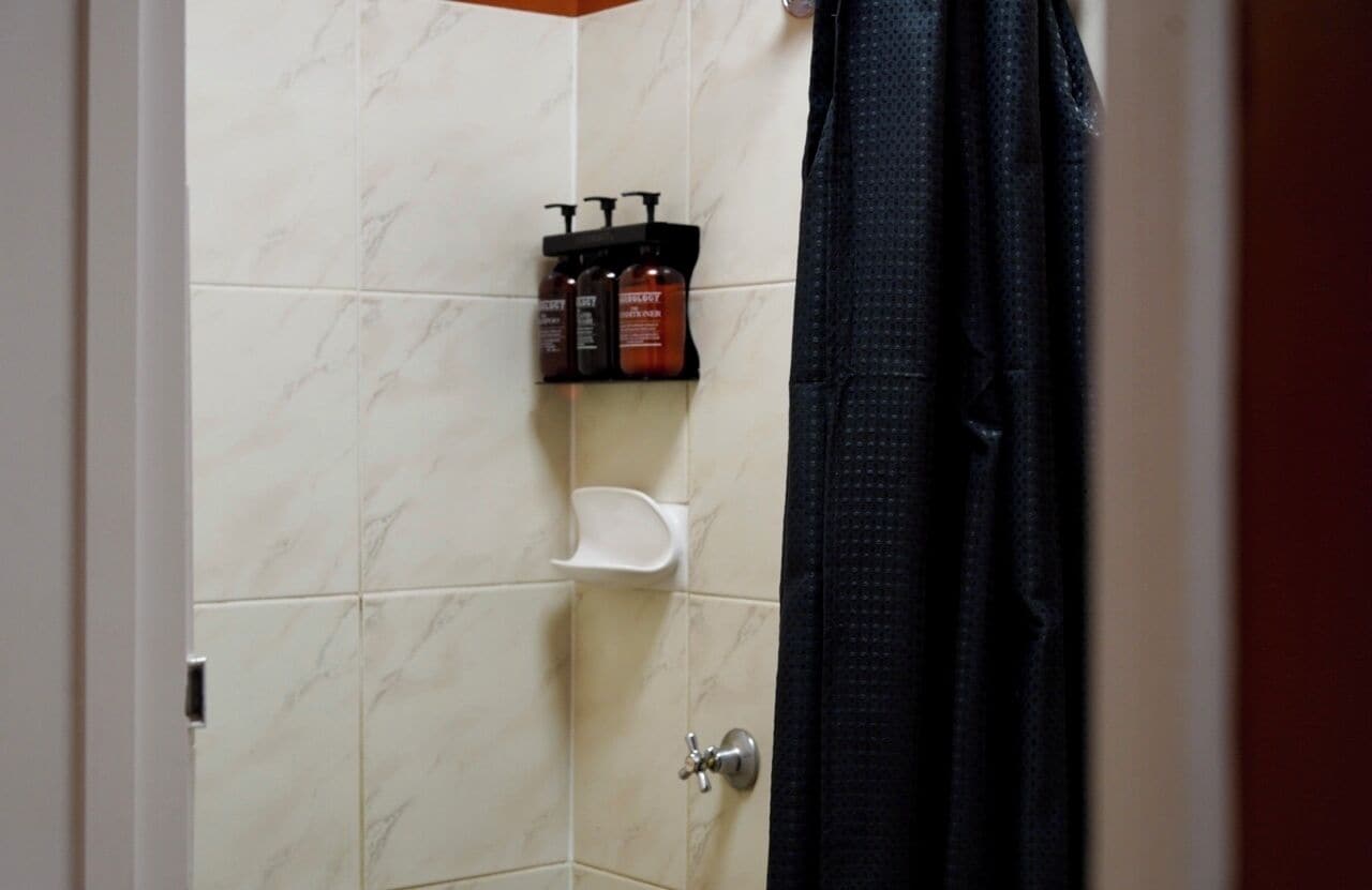 Un baño con ducha, inodoro y un estante con artículos de aseo.