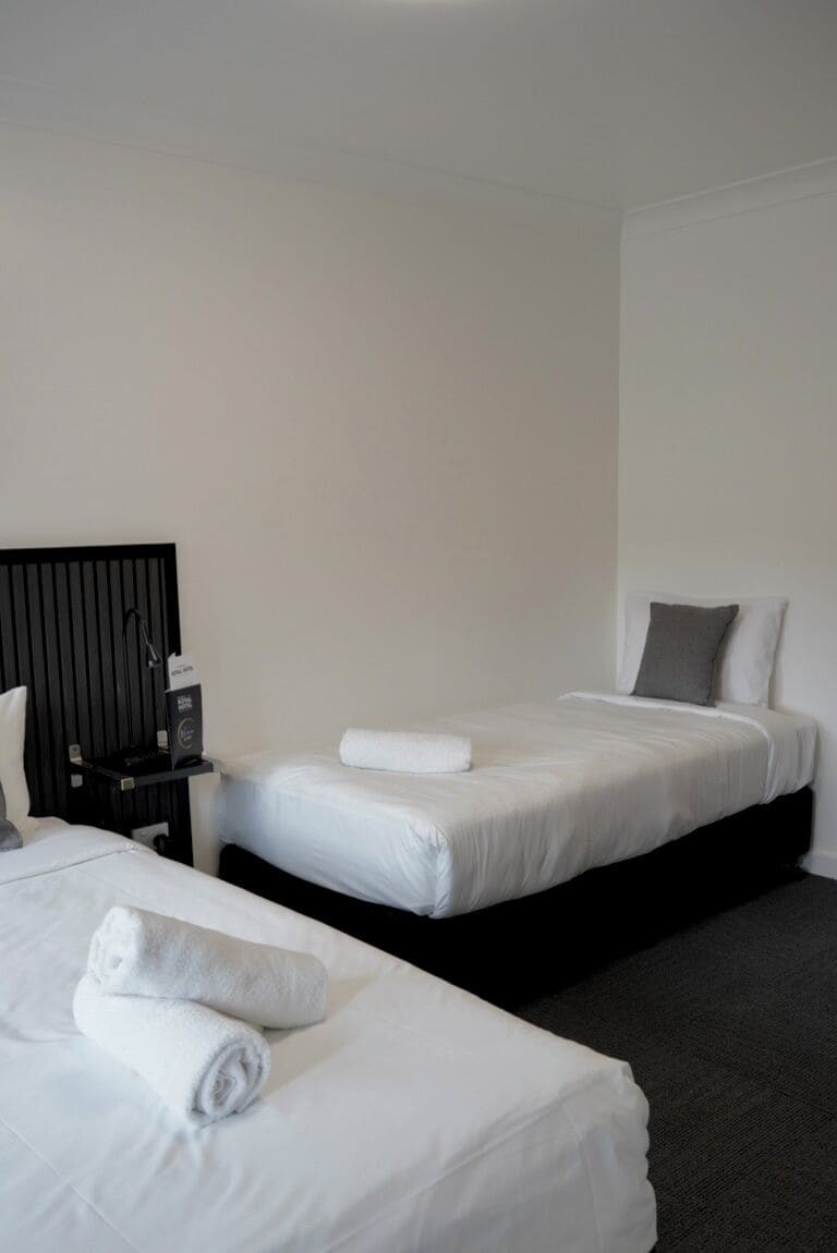 Een hotelkamer met twee bedden, een nachtkastje en een wandplank.