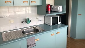 Una cocina con armarios azul claro, un lavamanos de acero inoxidable, un microondas, un hervidor y una tostadora.