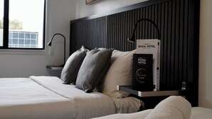 A modern hotel room with a bed, a nightstand, a lamp, and a framed picture on the wall.
