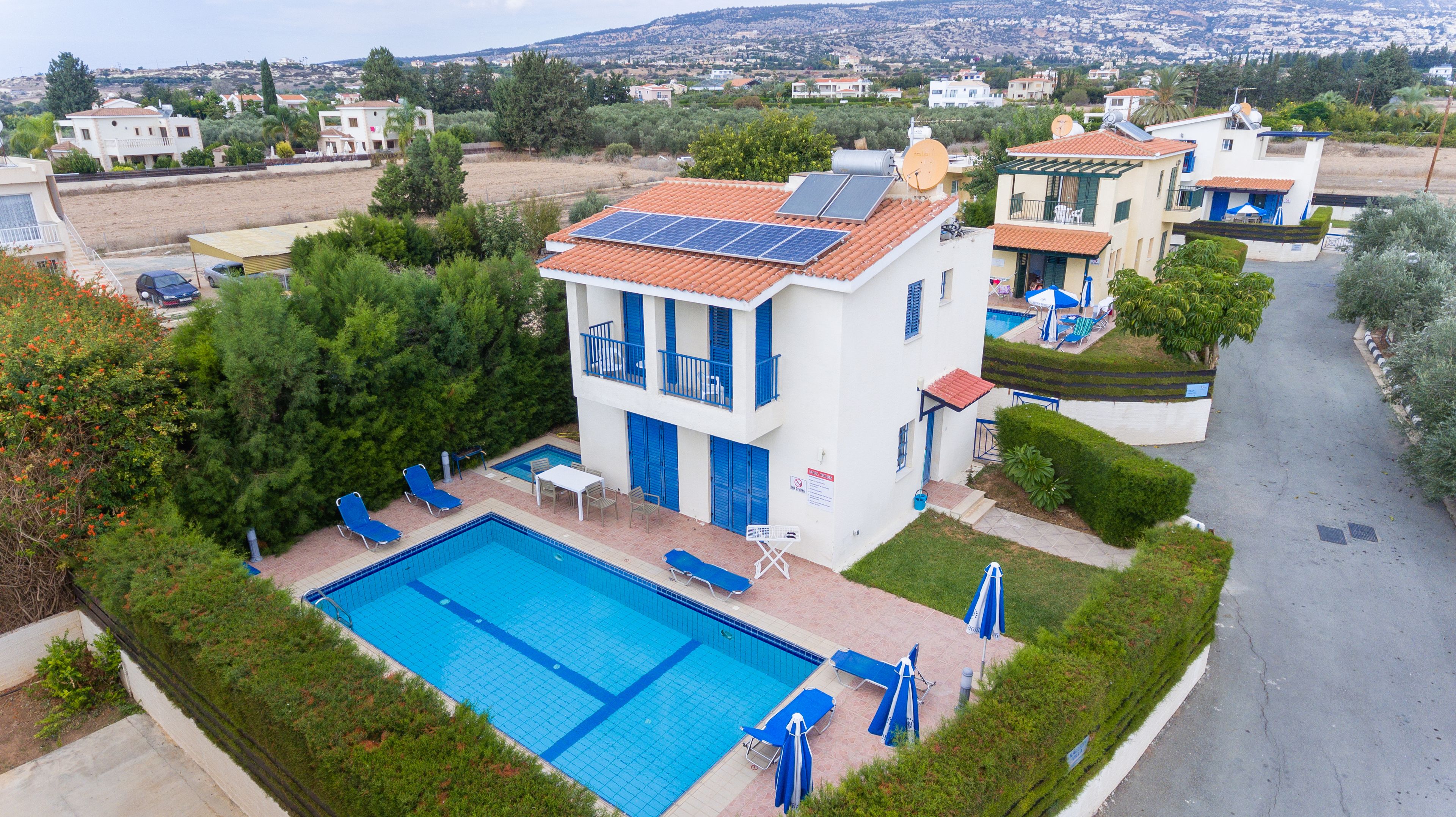 A residential building with a swimming pool, solar panels, and a view of a hillside.