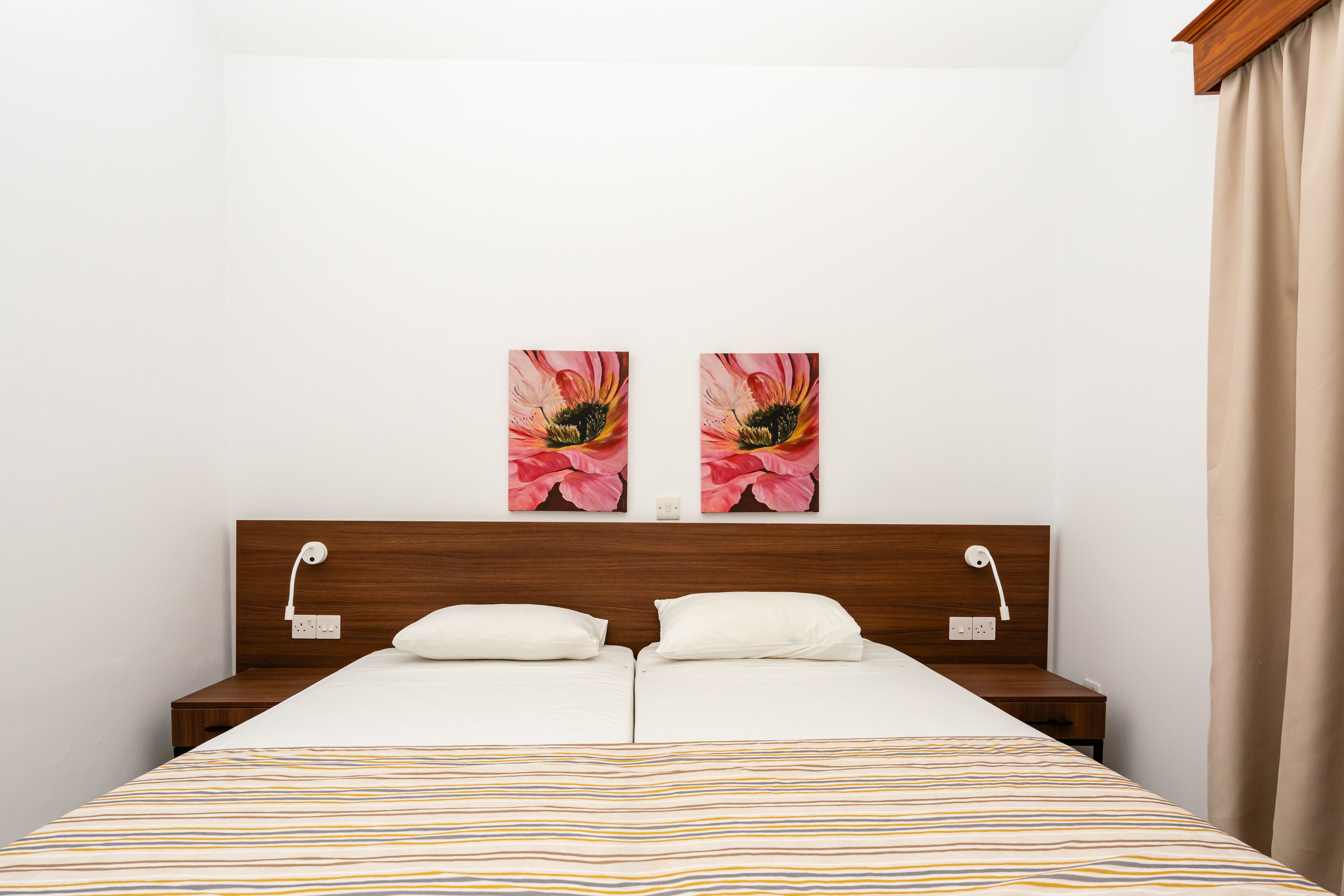 Ein Doppelbett mit gestreiftem Bettbezug, zwei Nachttische, ein Holz-Kopfteil und zwei Wandlampen.