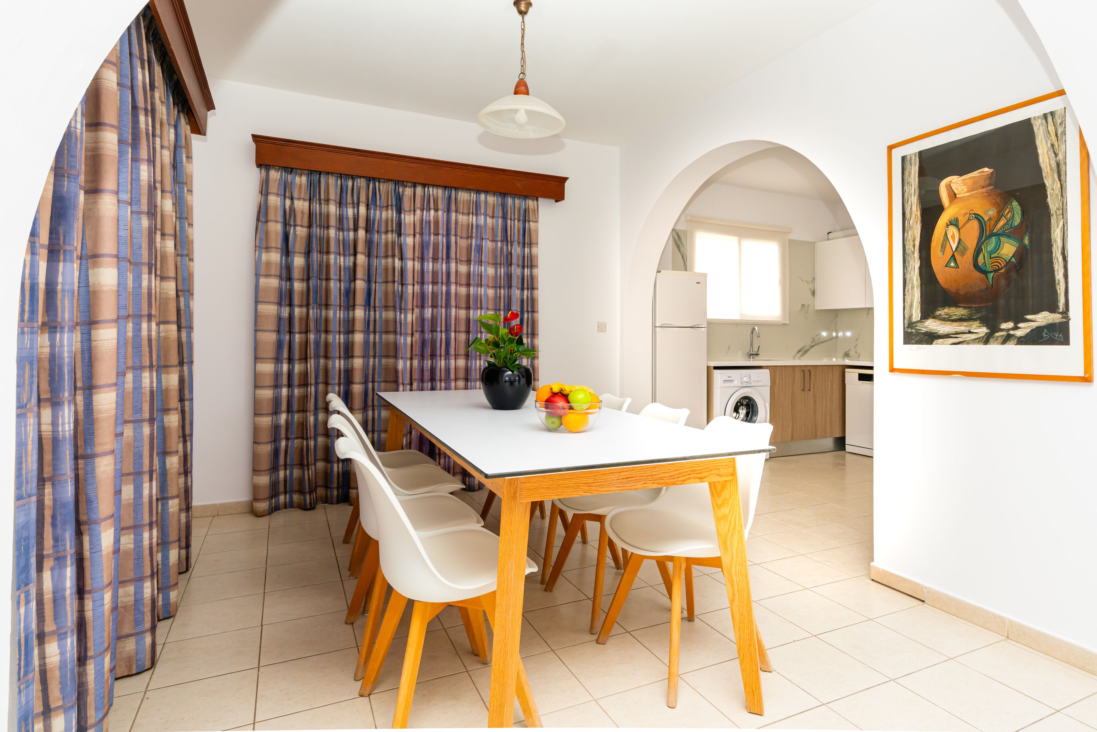 A dining area with a white table and wooden chairs, a potted plant, and a bowl of fruit.
