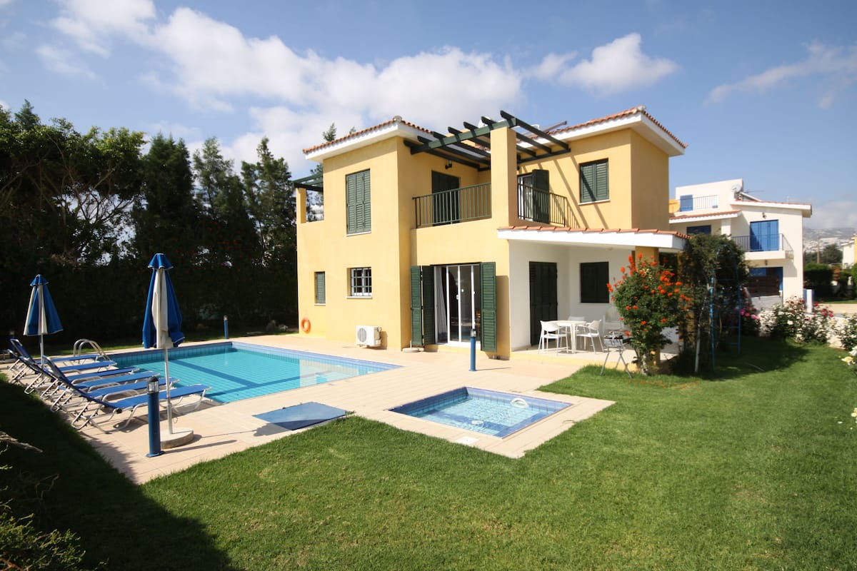 A two-story house with a swimming pool, a patio with lounge chairs, and a garden.