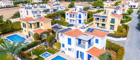 A residential area with multiple two-story houses, each with a swimming pool and solar panels.