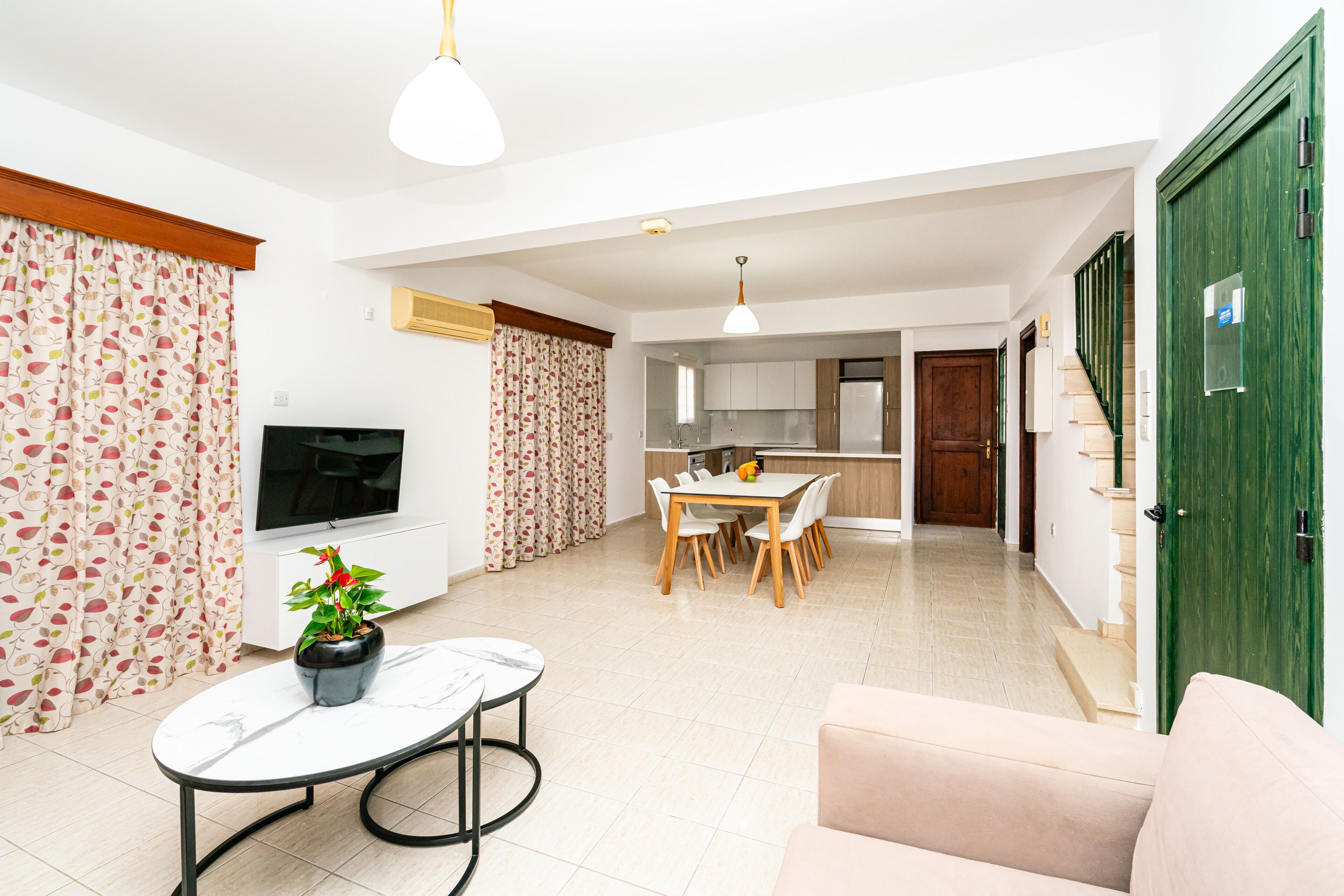 A modern living room with a TV, a dining area, and a kitchen.