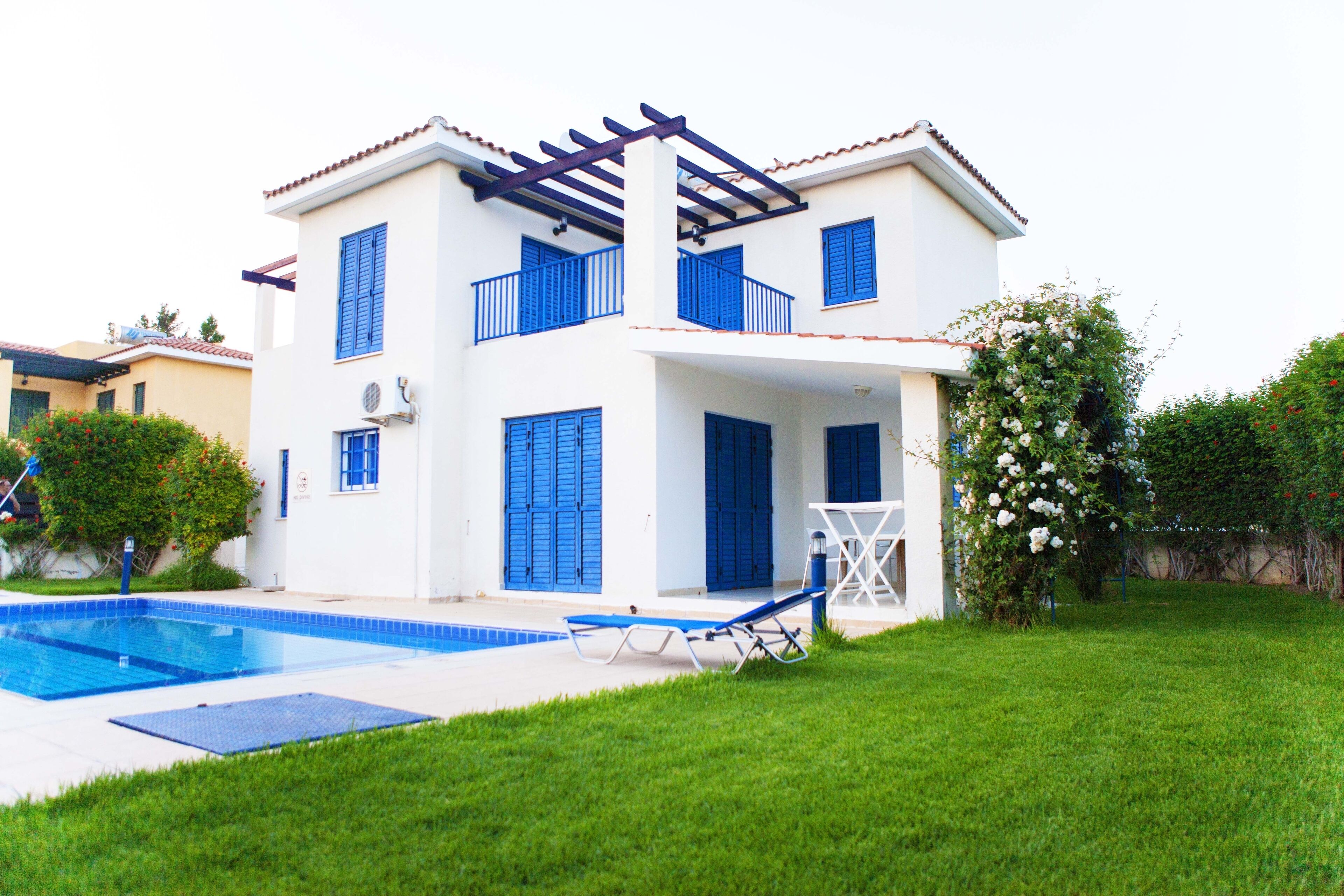 A two-story house with a swimming pool, blue shutters, and a pergola.