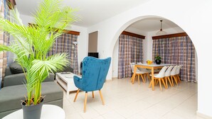 Un salon moderne avec un fauteuil bleu, une table à manger avec des chaises et une plante en pot.