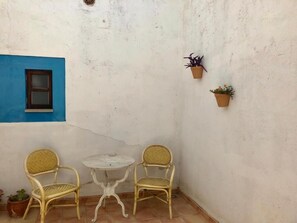 A small, enclosed patio area with two wicker chairs, a small round table, and two potted plants on the wall.