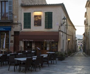 An outdoor cafe with tables and chairs, a building with a sign for 'Petit Hotel d'intérieur', and a street in the background.