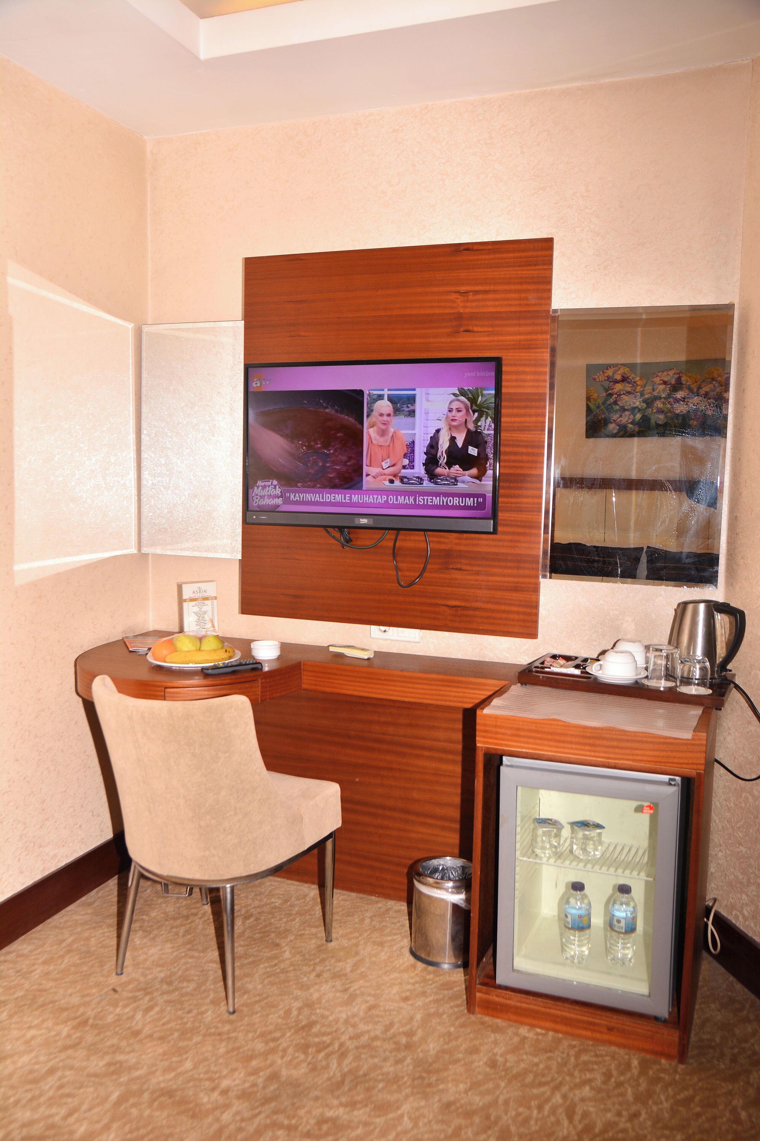 Habitación de hotel con televisión montada en la pared, refrigerador pequeño, escritorio con silla y ventana con vista.