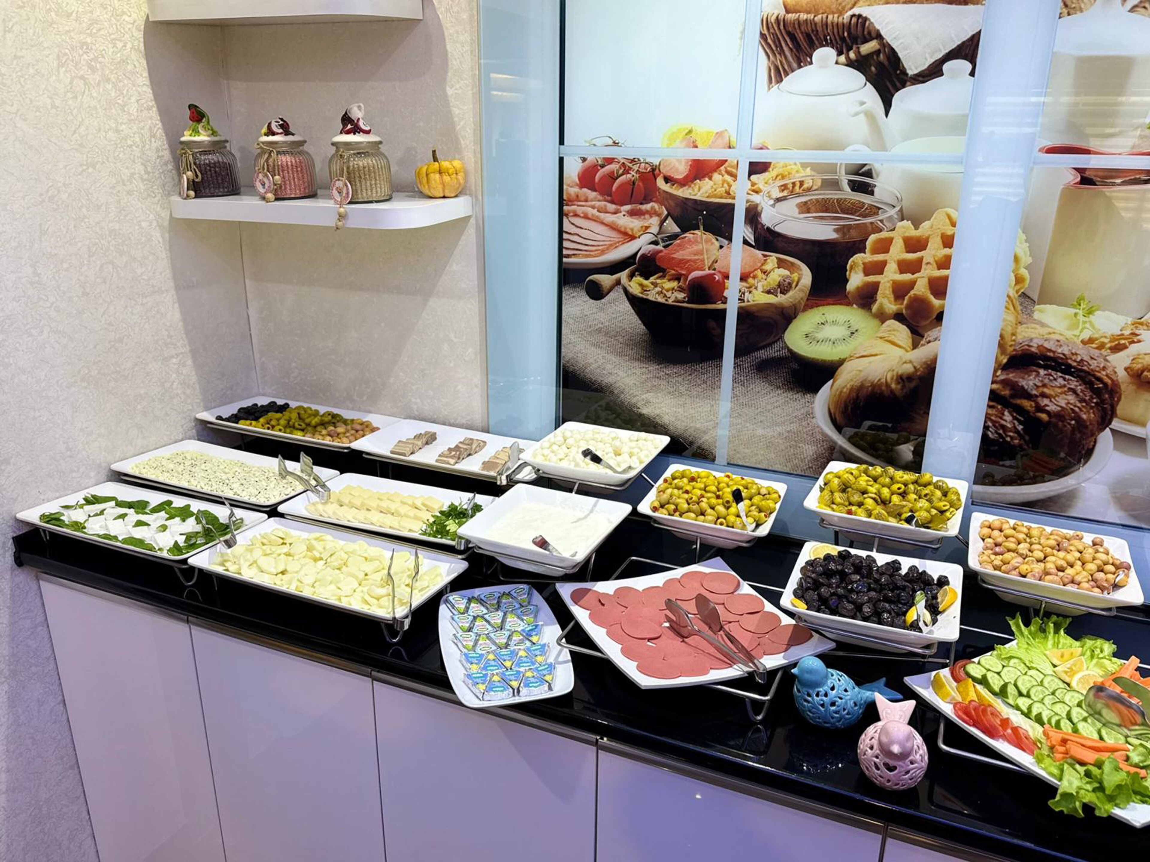 Un bufé con diversos alimentos, incluyendo quesos, aceitunas, carnes y verduras.