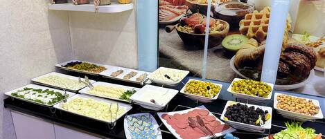 Un bufé con diversos alimentos, incluyendo quesos, aceitunas, carnes y verduras.