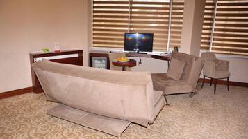 A living room with a sofa, two armchairs, a television, and a small table with a fruit bowl.
