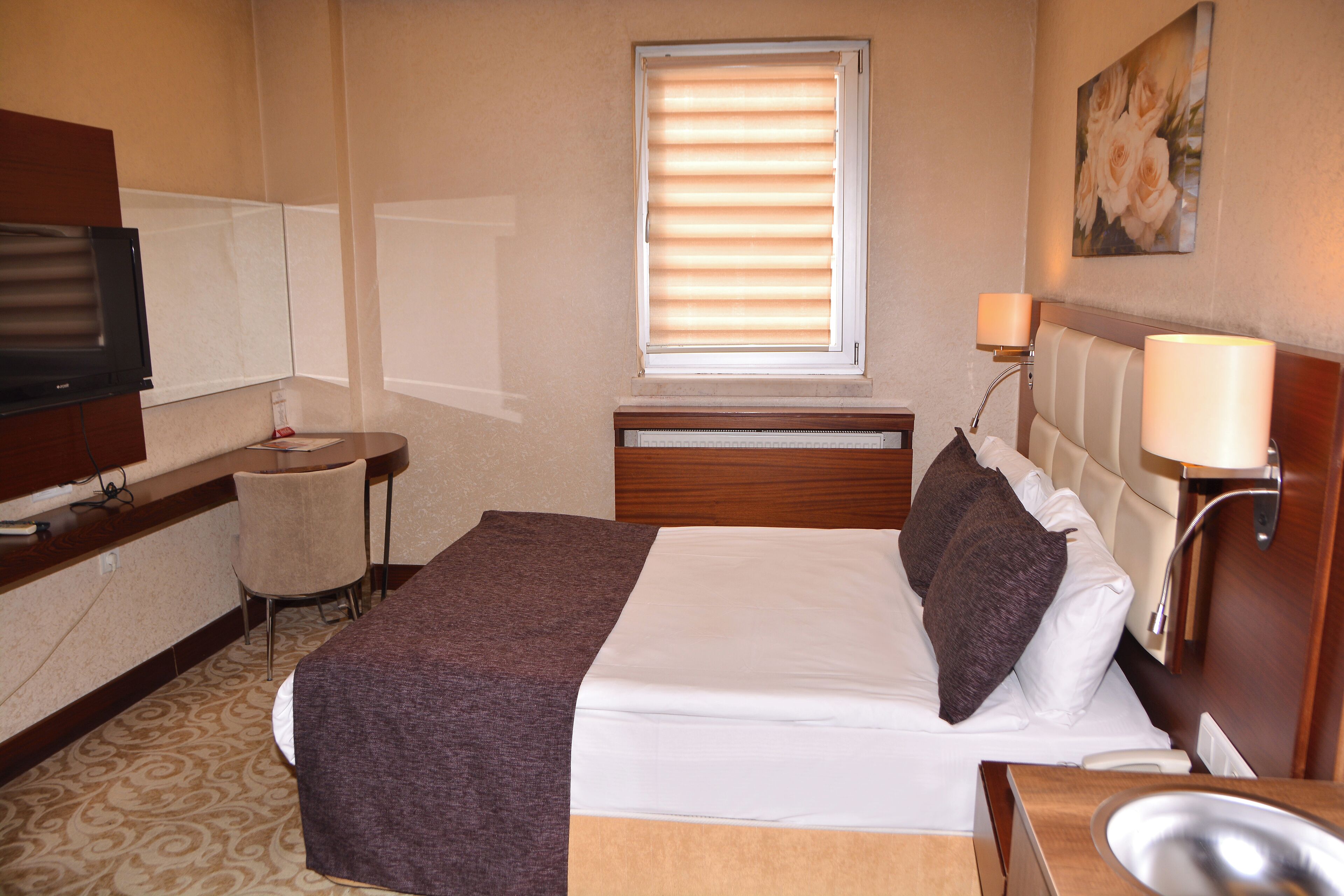 Een hotelkamer met een bed, nachtkastje, lamp, televisie en een klein bureau met stoel.