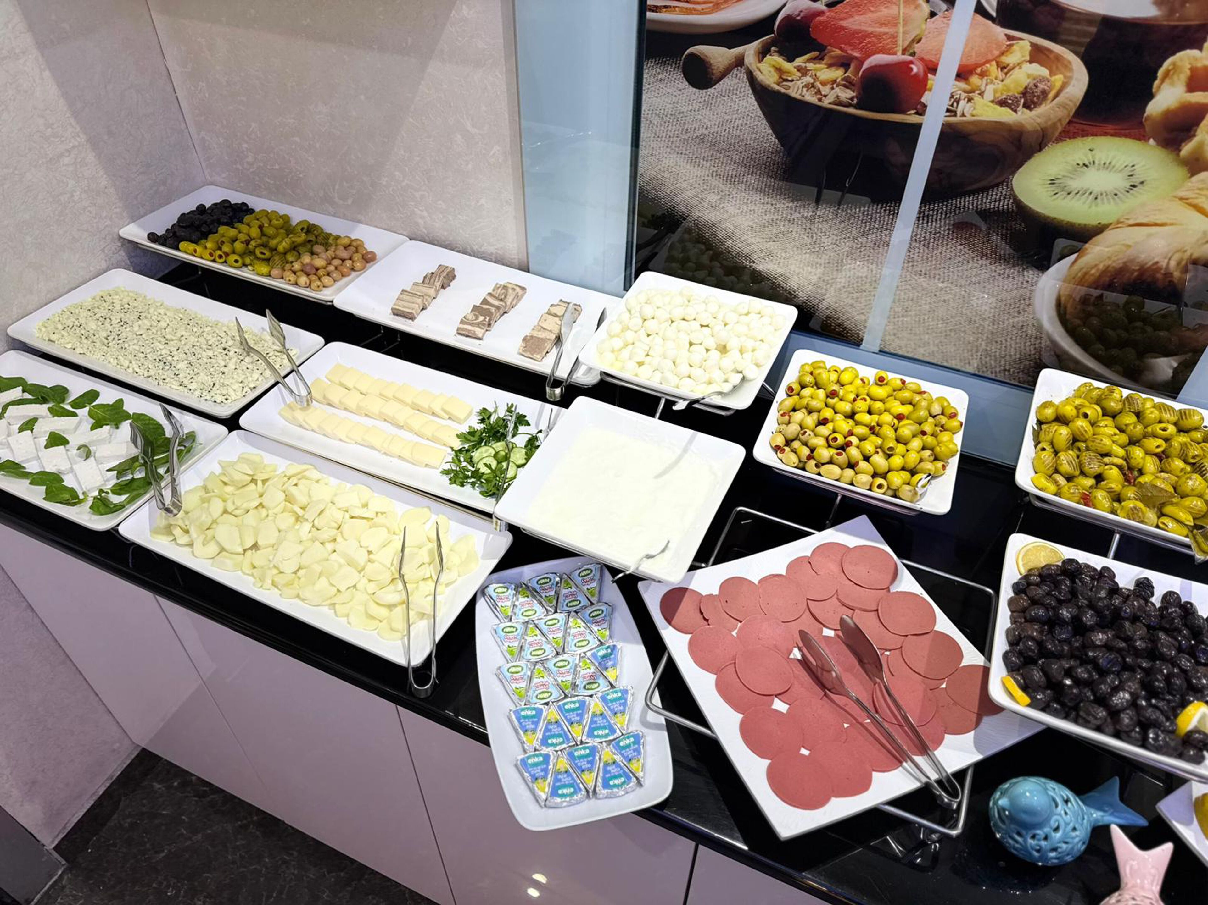 Un bufé con diferentes opciones de comida, incluyendo quesos, aceitunas y pasteles.