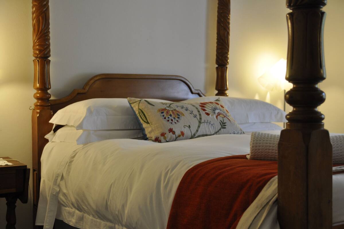 A four-poster bed with white linens and a red throw blanket.