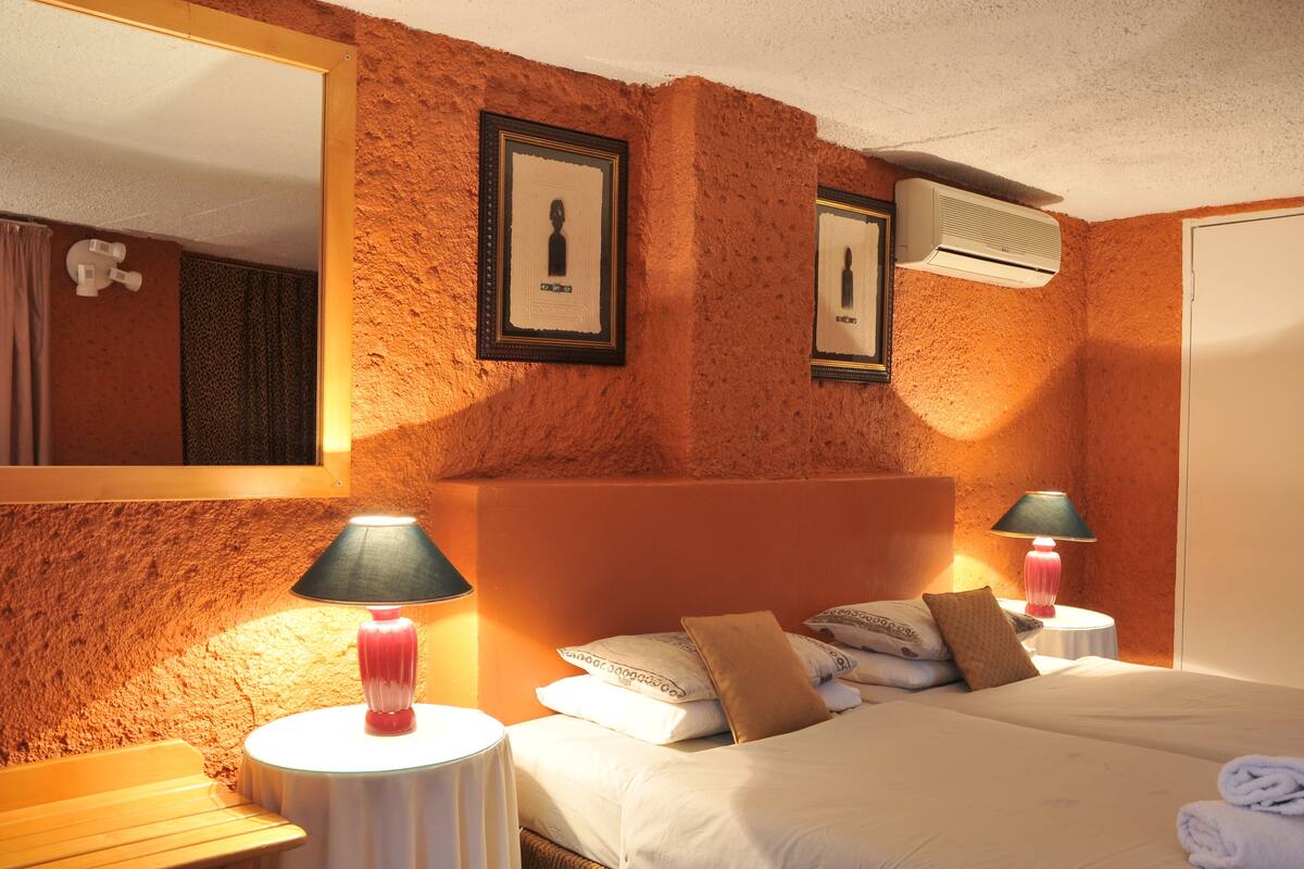 A hotel room with a textured orange wall, a large bed with white bedding, two bedside lamps, and framed pictures on the wall.