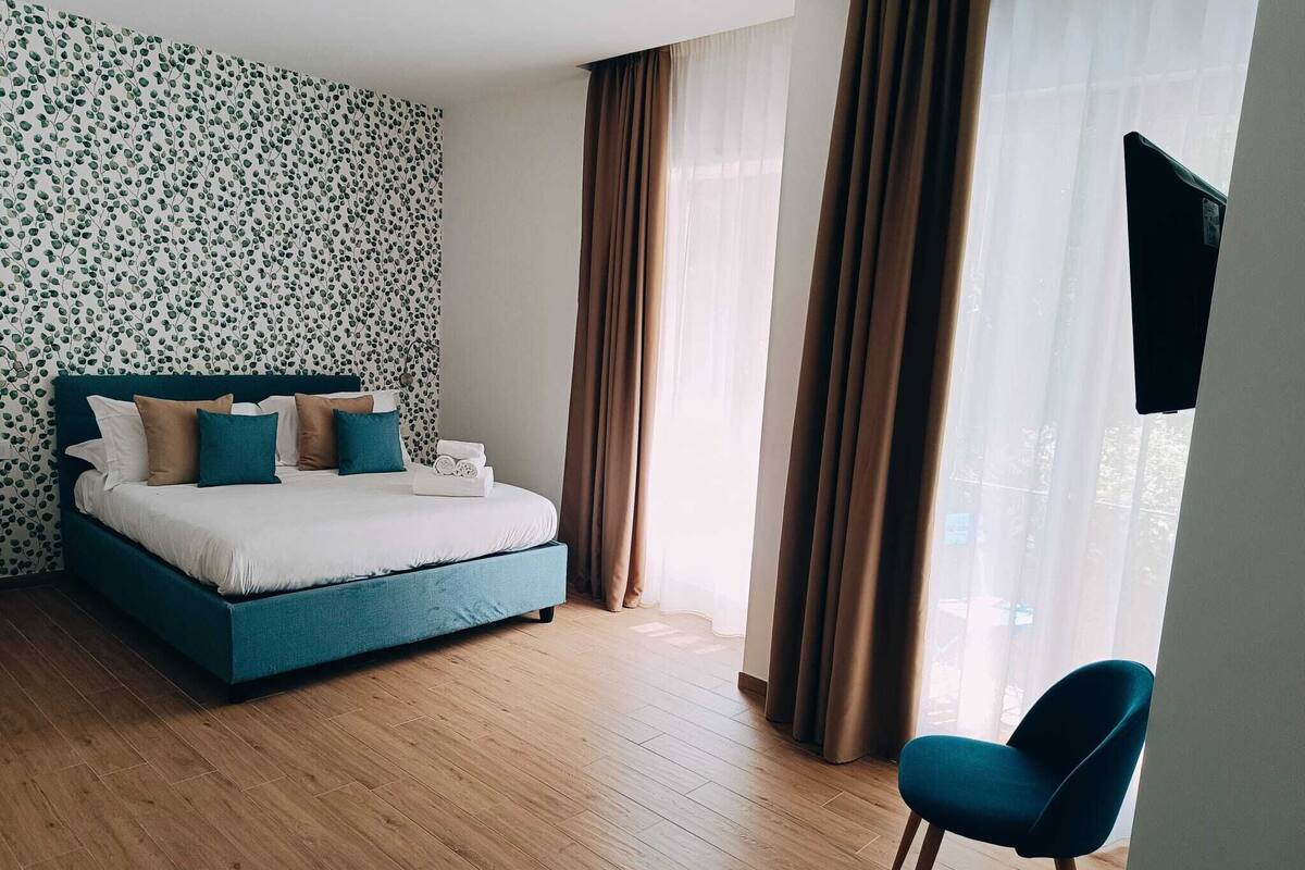 A hotel room with a bed, a chair, and a TV mounted on the wall.