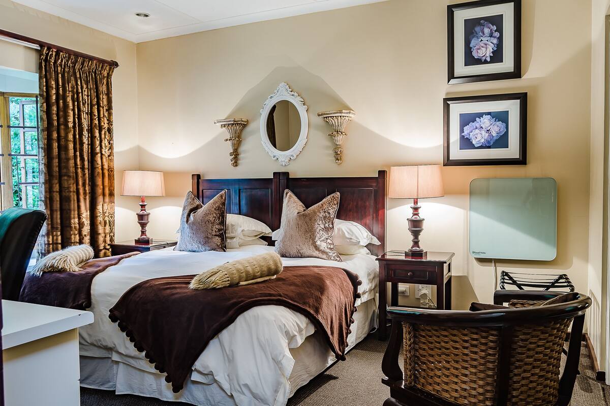 A well-appointed hotel room with a large bed, two bedside tables with lamps, a mirror, and framed floral artwork on the wall.