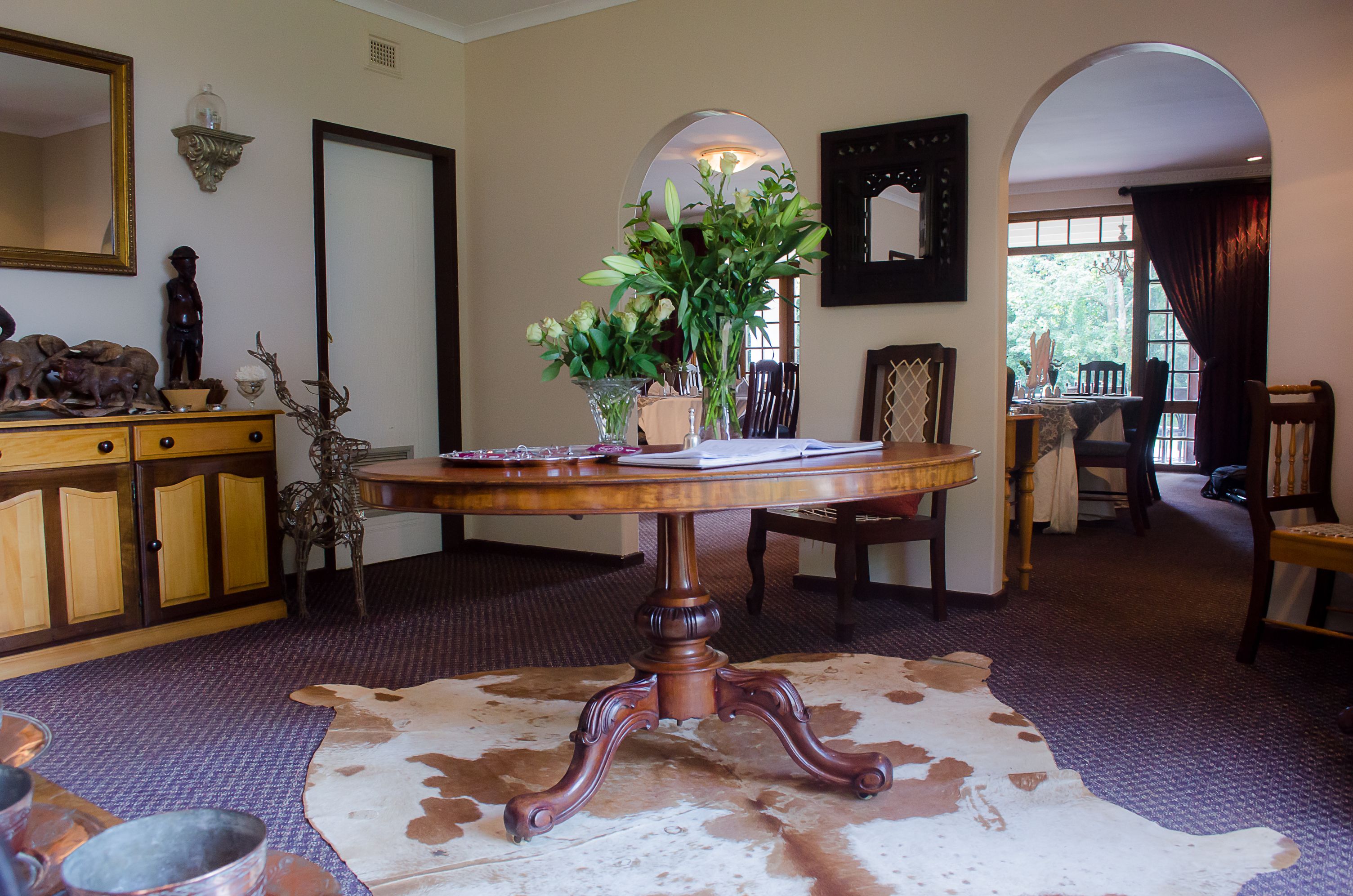 A dining area with a round table, chairs, a cowhide rug, and a wooden cabinet with decorative items.