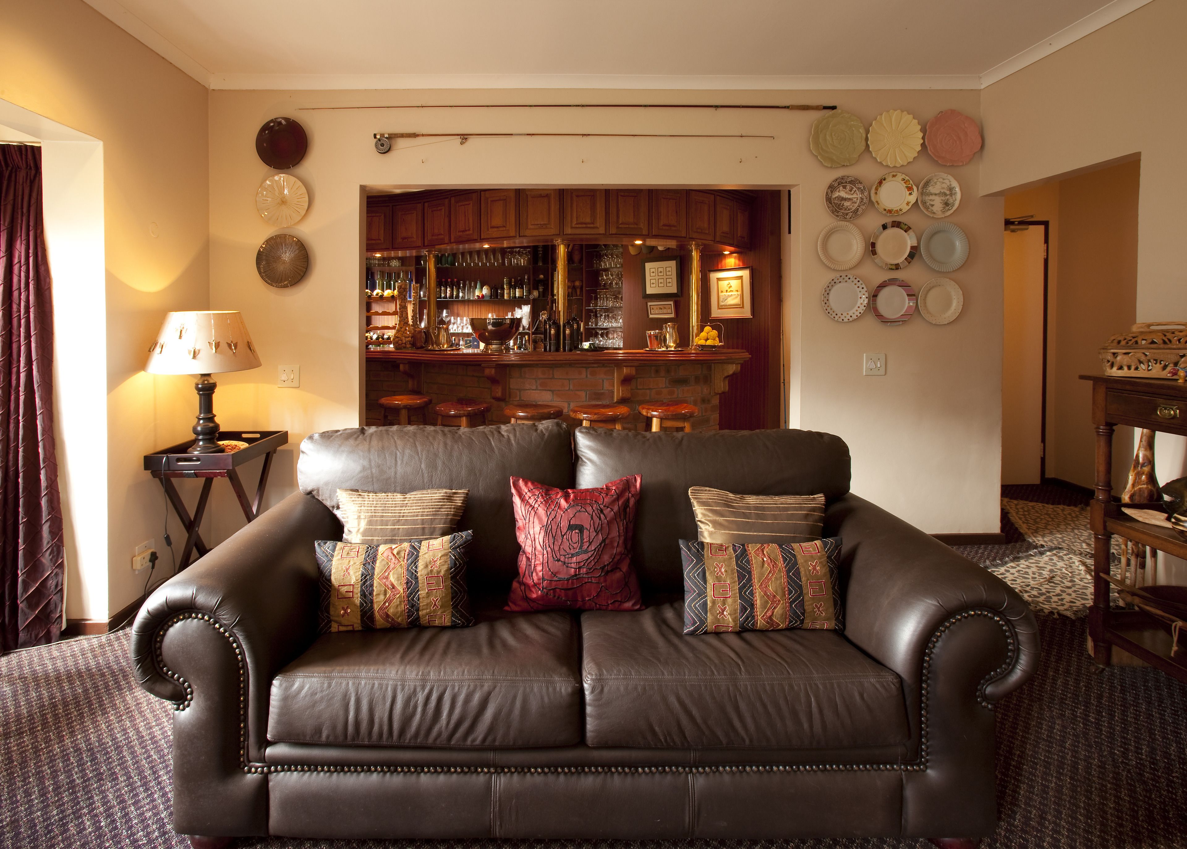 A living room with a leather sofa, a bar area with stools, and a wall decorated with plates.