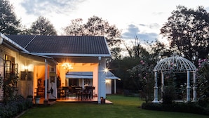 Een huis met een overdekte patio, een eethoek en een tuin met een vogelkooi.