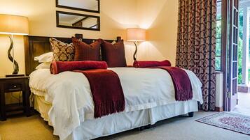 A neatly made bed with white and red bedding, two bedside lamps, a mirror above the bed, and a patterned curtain on a sliding door.