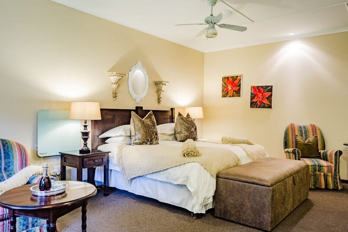 A hotel room with a large bed, a desk, a chair, a ceiling fan, and artwork on the walls.