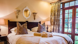 Een opgemaakt bed met een groot kussen, een bedlampje en een spiegel aan de muur.