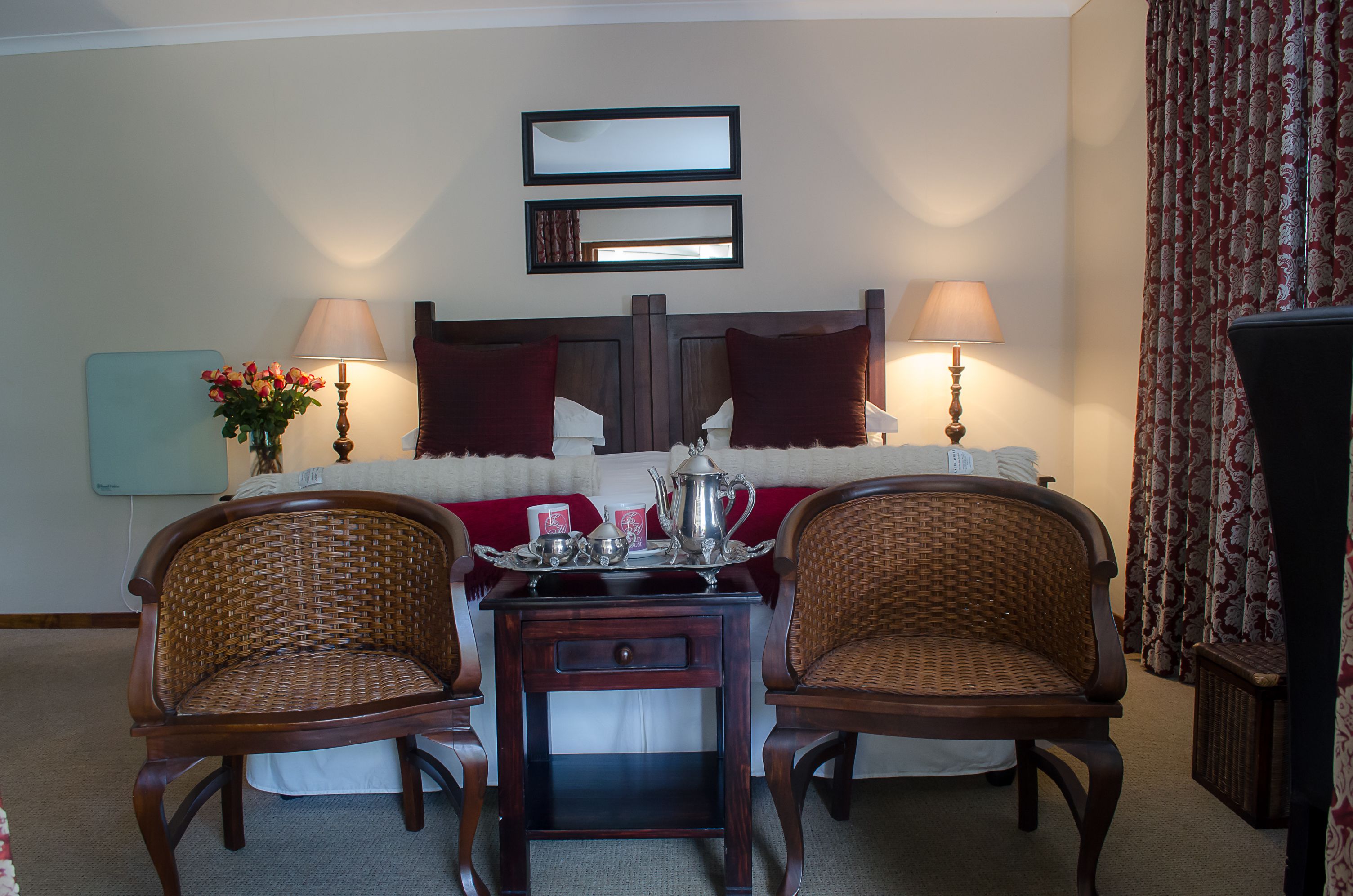 Habitación de hotel con cama, dos sillas, una mesita con bandeja, dos lámparas y un espejo en la pared.