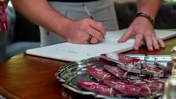 Una persona firmando un documento sobre una mesa de madera, con una bandeja de objetos y una ventana al fondo.